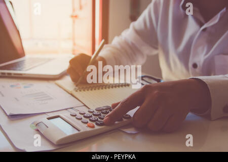 Man hand using a financial calculator with writing make note and Financial data analyzing on desk at home Stock Photo