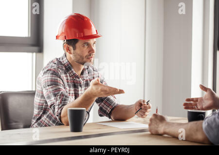 young ambitious builder is expressing his point of view on the problem while drinking coffee with colleague. close up side view photo Stock Photo