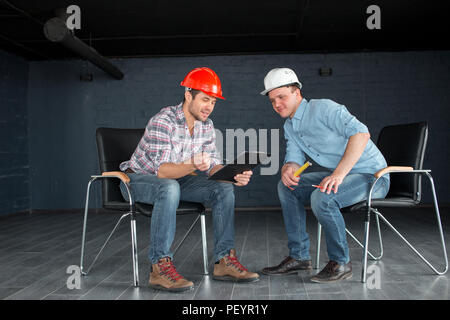 two talented workers in hardhats are looking at the documents indoors. full length photo Stock Photo