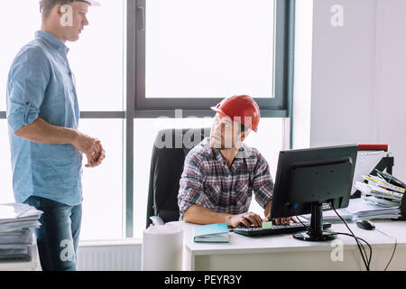 awesome constructor sitting in front of the computer is listening to the partner's advice in the office building Stock Photo