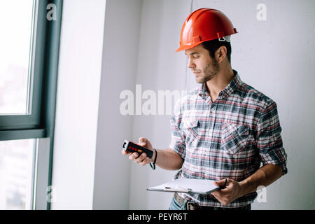 attractive builder is looking at the tape measure. close up side view photo. tools for building Stock Photo