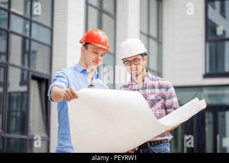 two hardworking builders are analyzing the project on the street with modern buildings Stock Photo