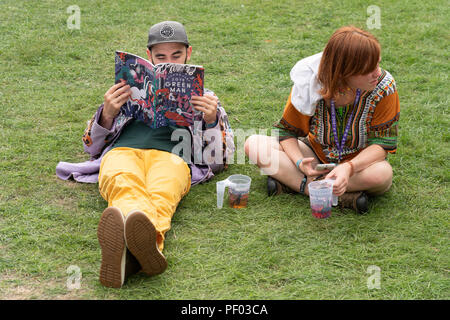 Glanusk Park, Brecon, Wales, 17th August 2018.  Day One of the Green Man music festival in the Brecon Beacons Mountains in Wales. A young couple sit in a quiet corner and check the line-up and running order hopefully there are no time clashes Credit: Rob Watkins/Alamy Live News Stock Photo