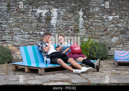 Glanusk Park, Brecon, Wales, 17th August 2018.  Day One of the Green Man music festival in the Brecon Beacons Mountains in Wales. A young couple sit in a quiet corner and check the line-up and running order hopefully there are no time clashes Credit: Rob Watkins/Alamy Live News Stock Photo