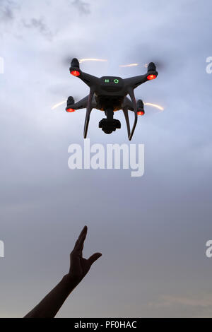 Hand catching drone aircraft in sunset sky background, camera operator of aerial photography Stock Photo