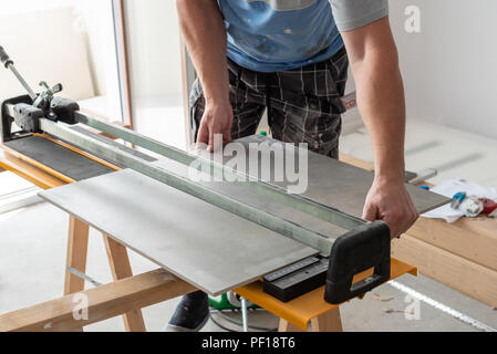 The man is cutting the floor tiles using a tile cutter machine.Home renovation. Stock Photo