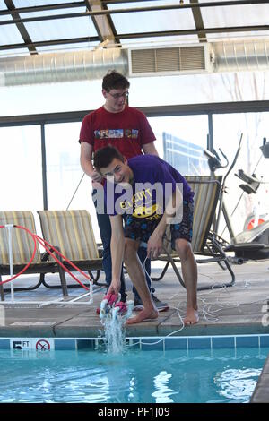 Two high school students retrieve a SeaPerch remotely operated underwater vehicle during a practice session at the Tierra Vista Community Center pool, Schriever Air Force Base, Colorado. Their team participates in the Challenger Colorado Regional Competition, completing obstacle courses and demonstrating engineering, navigation, and teamwork skills. The session highlights STEM education, robotics training, and preparation for competitive underwater robotics challenges among students. Stock Photo