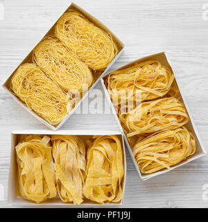 Set of various uncooked pasta in boxes on white wooden background, top view. Close-up. Stock Photo