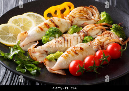 grilled squid with tentacles served with fresh vegetables close-up on a plate on a wooden table. horizontal Stock Photo
