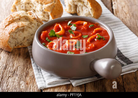stewed squid in tomato with spices, onion, pepper and parsley close-up in a bowl and fresh bread with olives on the table. horizontal Stock Photo