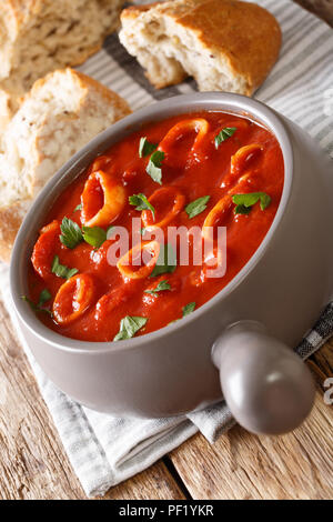 Italian thick tomato soup with squids close-up in a bowl, served with bread. vertical Stock Photo