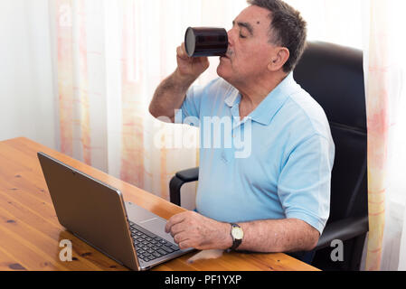 Senior man having a coffee and working on his computer Stock Photo