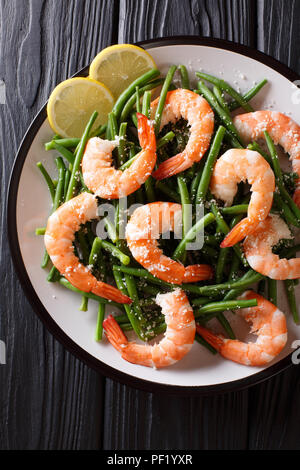 King prawns with green beans, cheese and lemon close-up on a plate on the table.Vertical top view from above Stock Photo