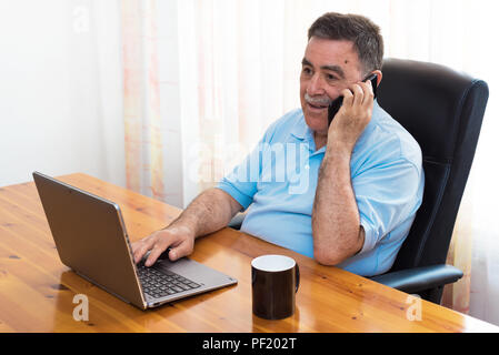 Cheerful Senior Man working on laptop while talking on the phone Stock Photo