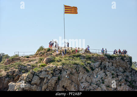 Tourists are near Senyera flag on the mast on top of Sa Palomera Rock in Blanes, Costa Brava coast in Catalonia, Spain. Stock Photo