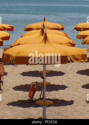 Calabria (Italy): deserted beach with a row of orange beach umbrellas, on a sunny summer day, waiting for customers Stock Photo