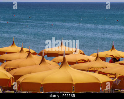 Calabria (Italy): orange beach umbrellas, lined up on the beach on a sunny summer day, with a beautiful blue sea in the background Stock Photo