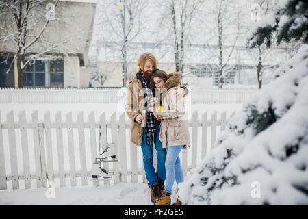 Young loving couple caucasian man with blond long hair and beard, beautiful woman have fun drinking a hot drink from thermos, eating green apple in sn Stock Photo