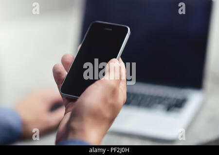 Cropped image of young woman downloading applications and multimedia programs by mobile smartphone, with laptop computer at street in modern city. Stock Photo