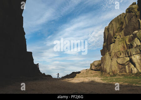 Teenager on phone in the countryside with a younger girl running, Ilkley Cow and Calf Rocks Stock Photo