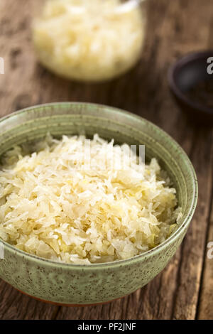 Fresh healthy sauerkraut in bowl with jar in the back, photographed on rustic wood (Selective Focus, Focus one third into the image) Stock Photo
