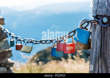 The metal locks hanging on a metal chain as a symbol of two people and their eternal love. Giant mountains on a background. Selective focus, small dep Stock Photo