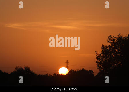 Setting Sun with an electric pylon in front of it Stock Photo