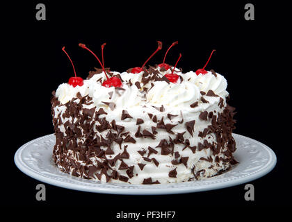 black forest cake on an off white plate isolated on a dark background. Whipped cream, shaved chocolate candy, cherries on top. Stock Photo