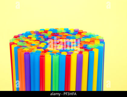 Hundreds of colorful plastic straws laying on yellow surface with yellow background facing open end up clustered in a round pattern. Many cities are n Stock Photo