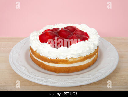 Light refreshing vanilla cake with cream filling, topped with whipped cream and glazed whole strawberries on a light wood table with light pink backgr Stock Photo