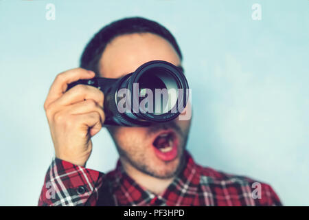 Surprised young man tourist holding photo camera. blue background. reporter makes an amazing shot. Photographer surprised by the picture. The paparazz Stock Photo