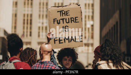 Woman's march protest sign that reads the future is female. Female walking on the city street holding a banner with group of people. Stock Photo
