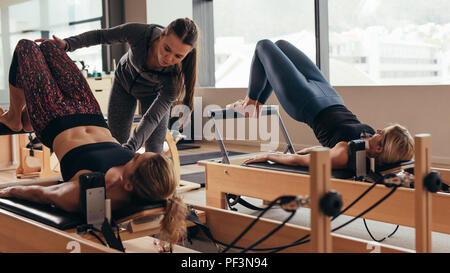 Pilates instructor training women at the gym. Two fitness women doing pilates workout on pilates equipment. Stock Photo