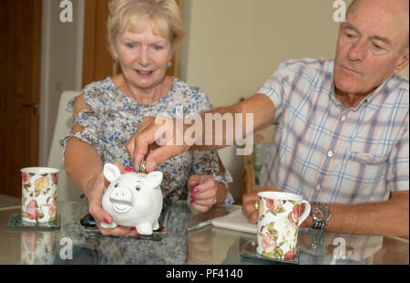 Elderly couple checking their expenditure and savings, Man placing money into piggy bank Stock Photo
