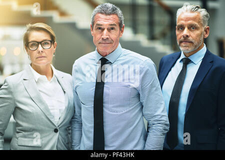 Confident mature businessman standing with two work colleagues in the lobby of a modern office building Stock Photo