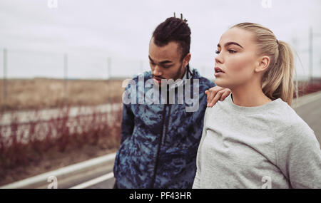 Diverse young couple in sportswear preparing to go for a jog together on a country road on an overcast day Stock Photo