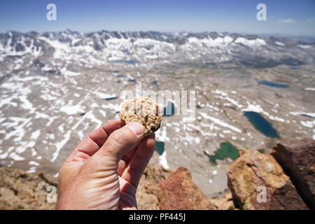 a mans hand holding a chocolate chip cookie on the summit of Mount Humphreys in the Sierra Nevada of California Stock Photo