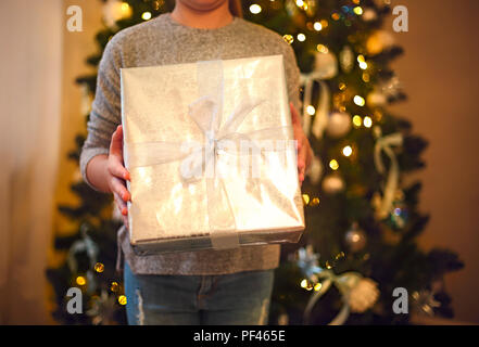 Little girl holding a Christmas silver present near the Christmas tree. Christmas holiday concept Stock Photo