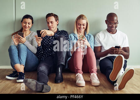 Group of diverse young businesspeople sitting together on an office floor using their cellphones during breaktime Stock Photo