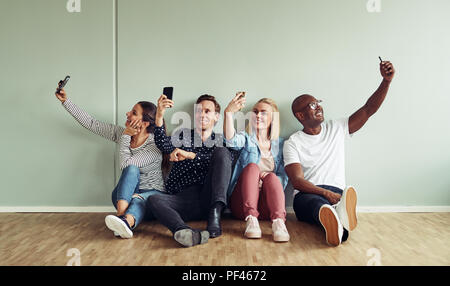 Group of diverse young colleagues sitting together on an office floor taking selfies while on their break in an office Stock Photo