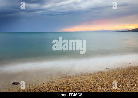 Colorful sunset and dark, stormy clouds over silky sea water of Paradisos beach in Neos Marmaras Stock Photo