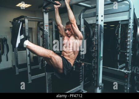 Fitness man hanging on horizontal bar performing legs raises, in the gym Stock Photo