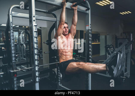 Fitness man hanging on horizontal bar performing legs raises, in the gym Stock Photo