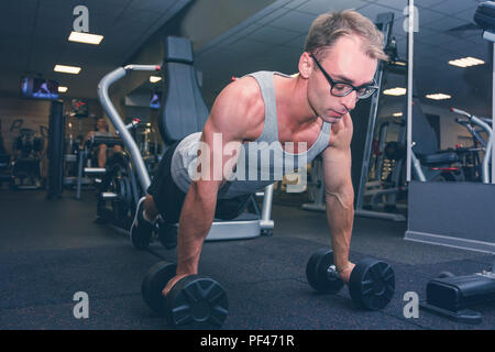 Strong man doing push-ups exercises on dumbbells Stock Photo