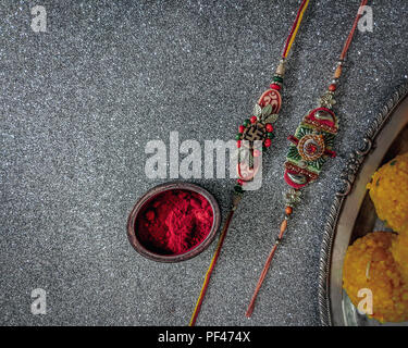 Rakhi with rice grains, kumkum and sweets on decorative plate and background with elegant Rakhi. A traditional Indian wrist band, symbol of love betwe Stock Photo