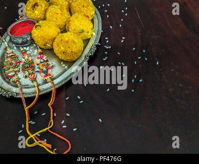 Rakhi with rice grains, kumkum and sweets on decorative plate and background with elegant Rakhi. A traditional Indian wrist band, symbol of love betwe Stock Photo