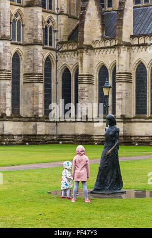 Two young girls looking at the walking Madonna statue and lamp in front of Salisbury Cathedral at Salisbury, Wiltshire UK on a wet rainy day in August Stock Photo