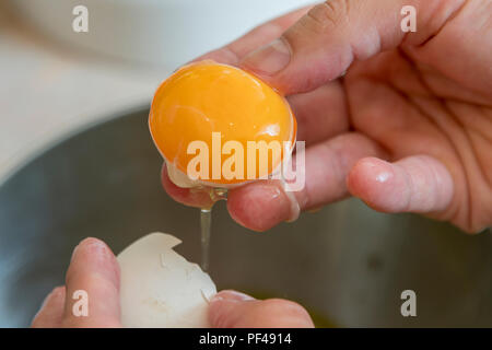 Female hands separate the egg white from the yolk over a bowl in the kitchen. the cook separates the yolk in the egg. Stock Photo