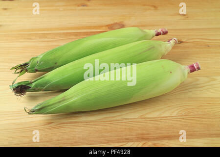 Three fresh purple corns with bright green husks and silks isolated on wooden background Stock Photo