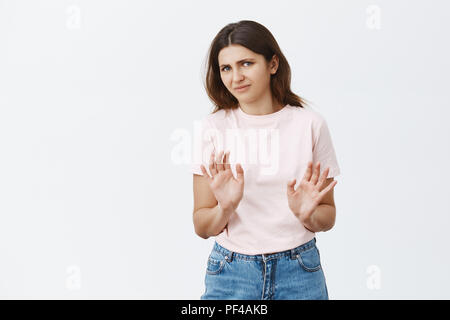 No thanks I refuse. Portrait of displeased unhappy and intense brunette female in pink t-shirt waving palms near chest in refusal or rejection gesture smiling bothered and unhappy over gray background Stock Photo
